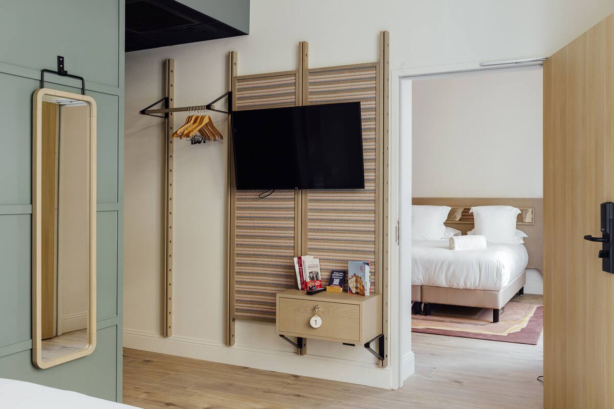 A bedroom with a bed, a TV mounted on a wall, a bedside table with a book, and a wardrobe with a mirror.
