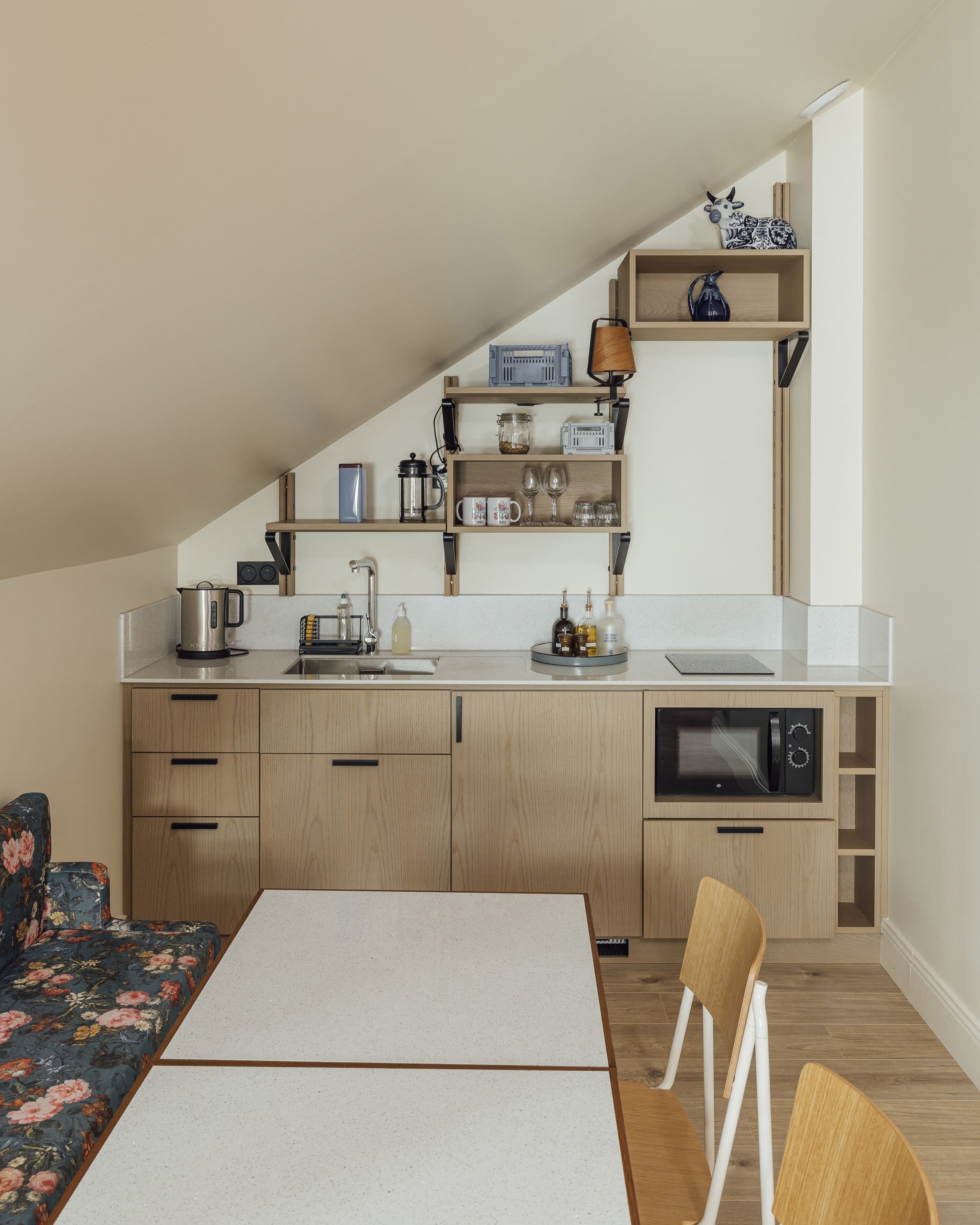 A compact kitchen with wooden cabinets, a microwave, and a coffee maker. There is a dining table with chairs and a sofa with floral upholstery.