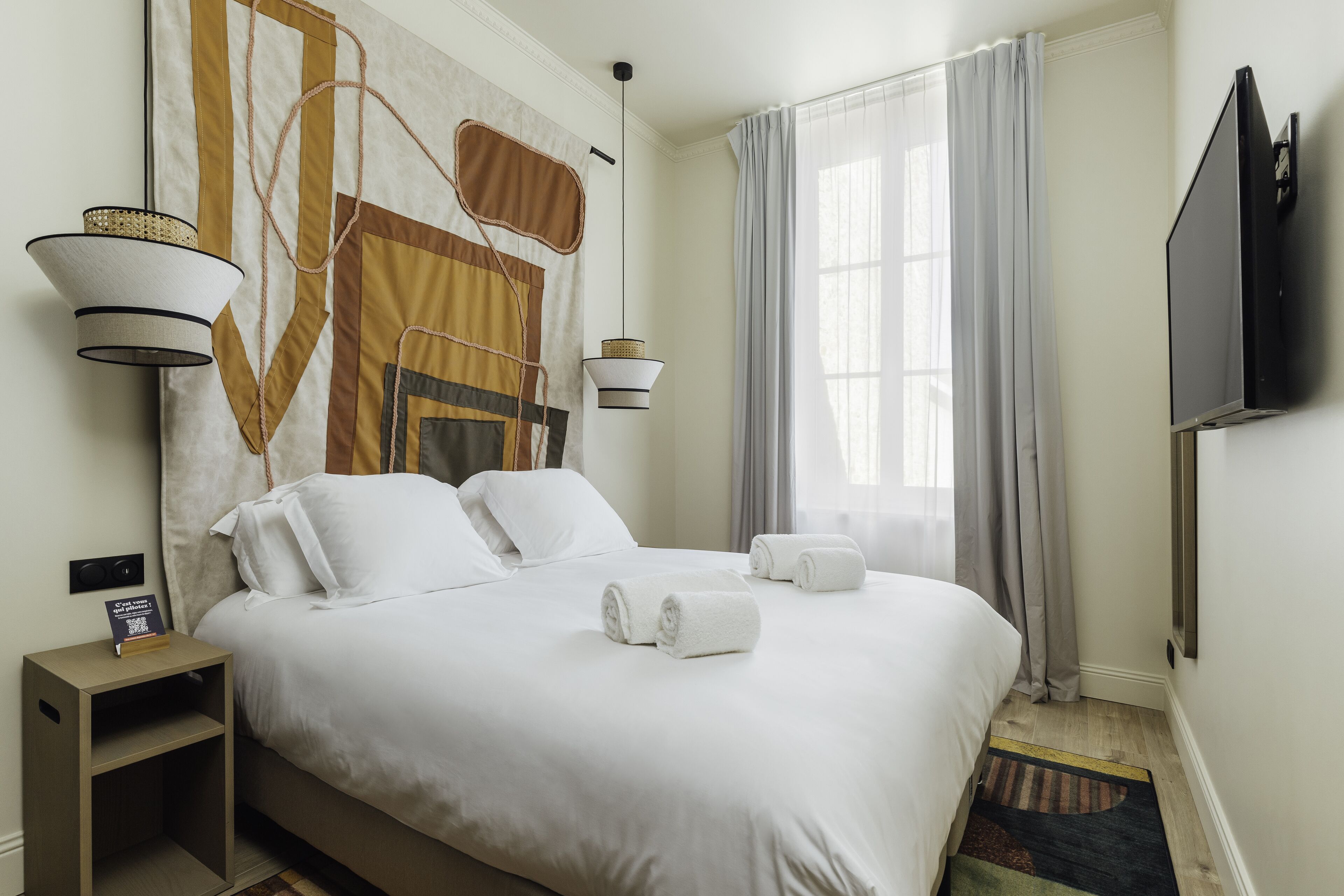 Habitación de hotel con una cama grande, dos lámparas de noche, un televisor de pantalla plana y un ventanal con cortinas.