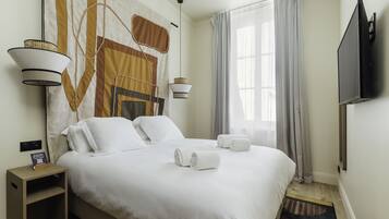 Habitación de hotel con una cama grande, dos lámparas de noche, un televisor de pantalla plana y un ventanal con cortinas.