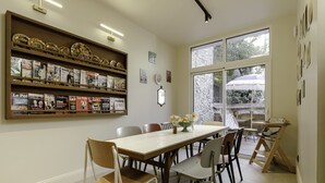 A dining area with a long table, chairs, and a bookshelf with magazines. - Hôtel Préfecture - 100m de l'Opéra - Encore Mieux (Limoges)