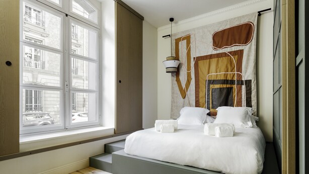 A bedroom with a large window, a bed with white linens, and a unique wall tapestry. - Hôtel Préfecture - 100m de l'Opéra - Encore Mieux (Limoges)