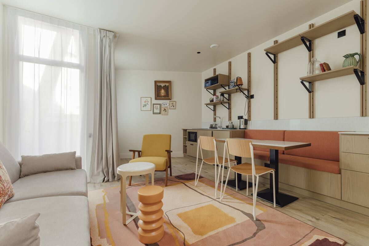 A modern living room with a sofa, chairs, a dining table, and a kitchen area with shelves.