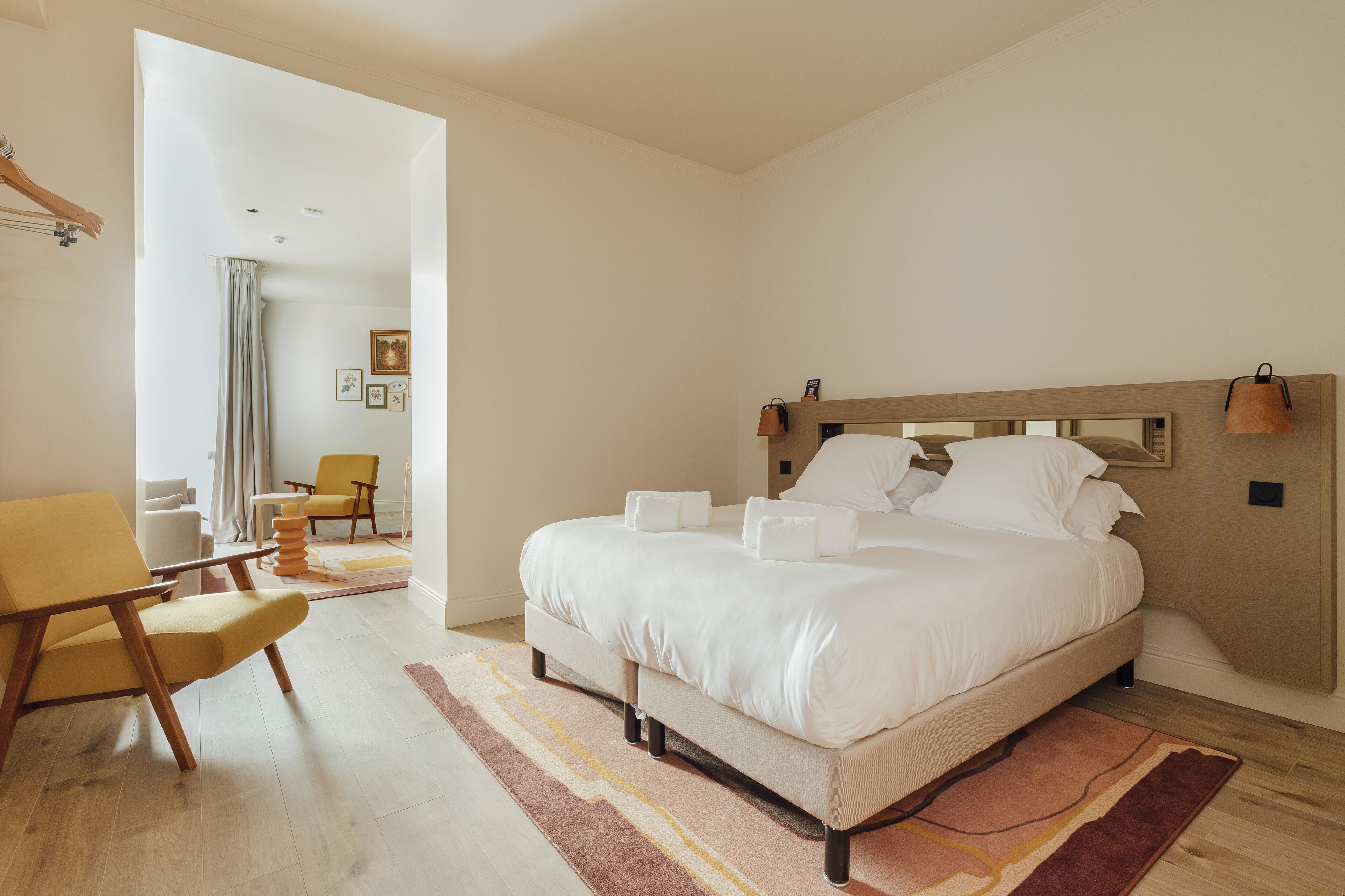A modern bedroom with a large bed, a wooden headboard, a chair, and a view of the living area.