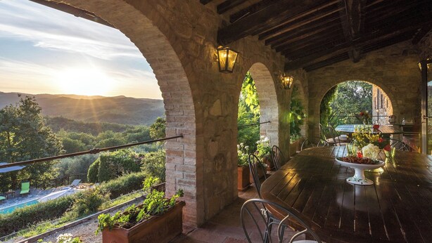 A terrace with a wooden table and chairs, stone arches, and a view of the landscape. - Podere Le Corone 14, Emma Villas (Perugia)