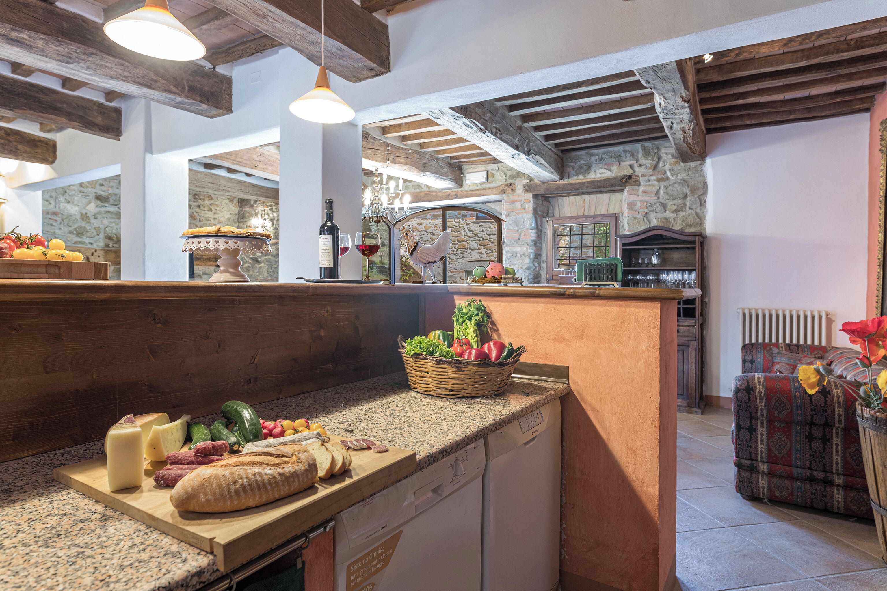 Une cuisine dotée de plans de travail en granit, de poutres en bois, de murs en pierre, d’une cheminée en pierre et d’un coin repas avec des meubles recouverts d’un tissu à motifs.