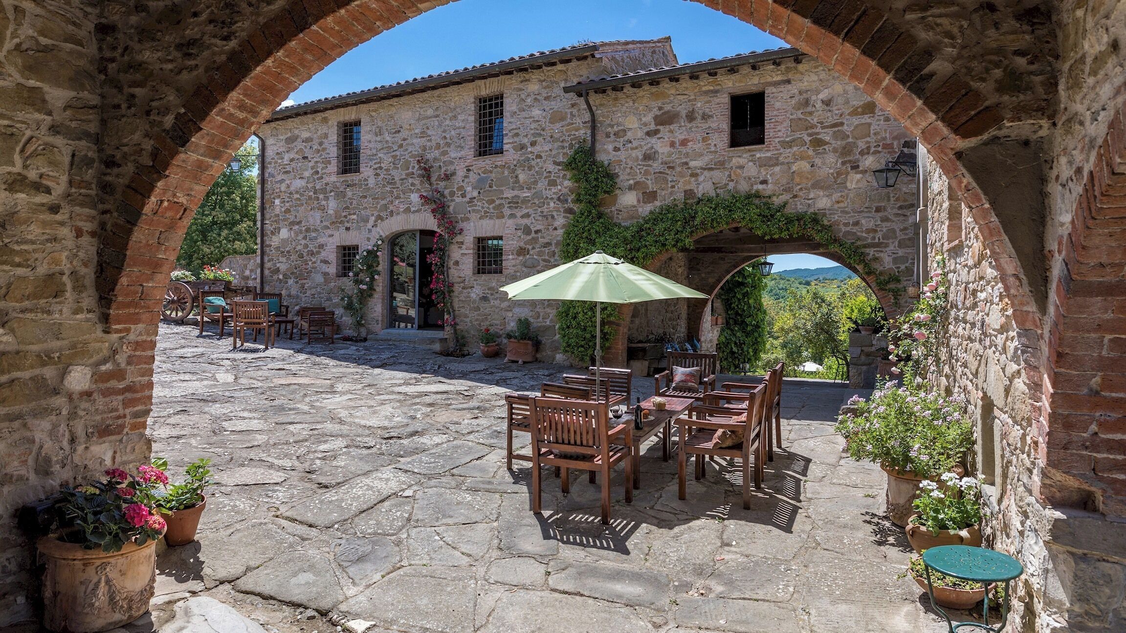 An outdoor patio with stone flooring, wooden furniture, and potted plants.