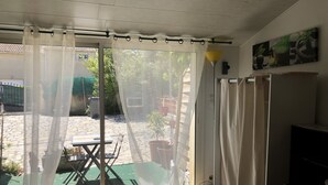 A room with a large window, a curtain, a table, and a chair. - 1 Bedroom Apartment in Tresques (Tresques)