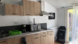 A modern kitchen with wooden cabinets, a built-in stove, a coffee maker, and a green dish rack. - 1 Bedroom Apartment in Tresques (Tresques)