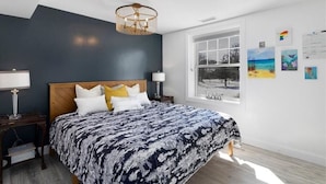 Une chambre avec un grand lit, une fenêtre donnant sur un beau paysage et des œuvres d’art accrochées au mur.