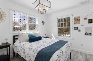 A bedroom with a large bed, two windows, a chandelier, and wall decorations.