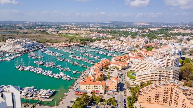 A marina with numerous boats docked, surrounded by residential buildings with red-tiled roofs.