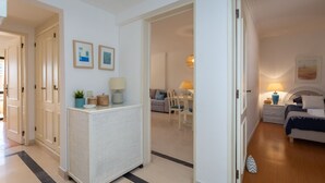 A hotel room with a bed, bedside table, lamp, and a view of the hallway.