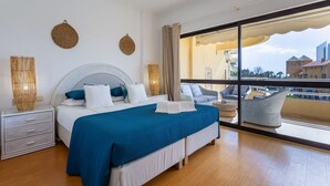 A modern hotel room with a large bed, a nightstand, a chair, and a view of the city through large windows.