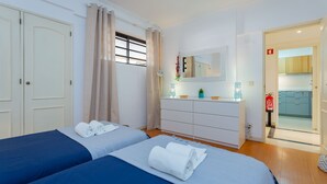 A hotel room with two beds, a dresser, a mirror, and a view of the kitchen.