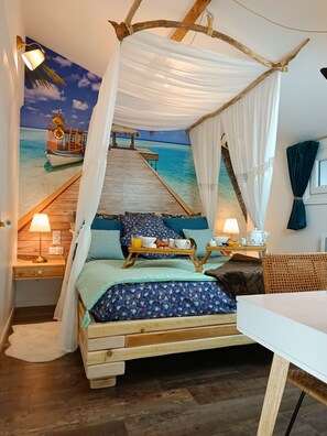 A bedroom with a bed under a canopy, a wooden desk, a nightstand, and a mural of a beach scene. - Cozy apartment with a whirlpool tub in the bedroom and a catamaran hammock (Caen)