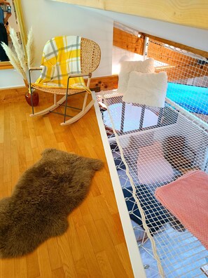 Ein gemütliches Zimmer mit Schaukelstuhl, Hängematte und weichem Teppich auf Holzdielen.