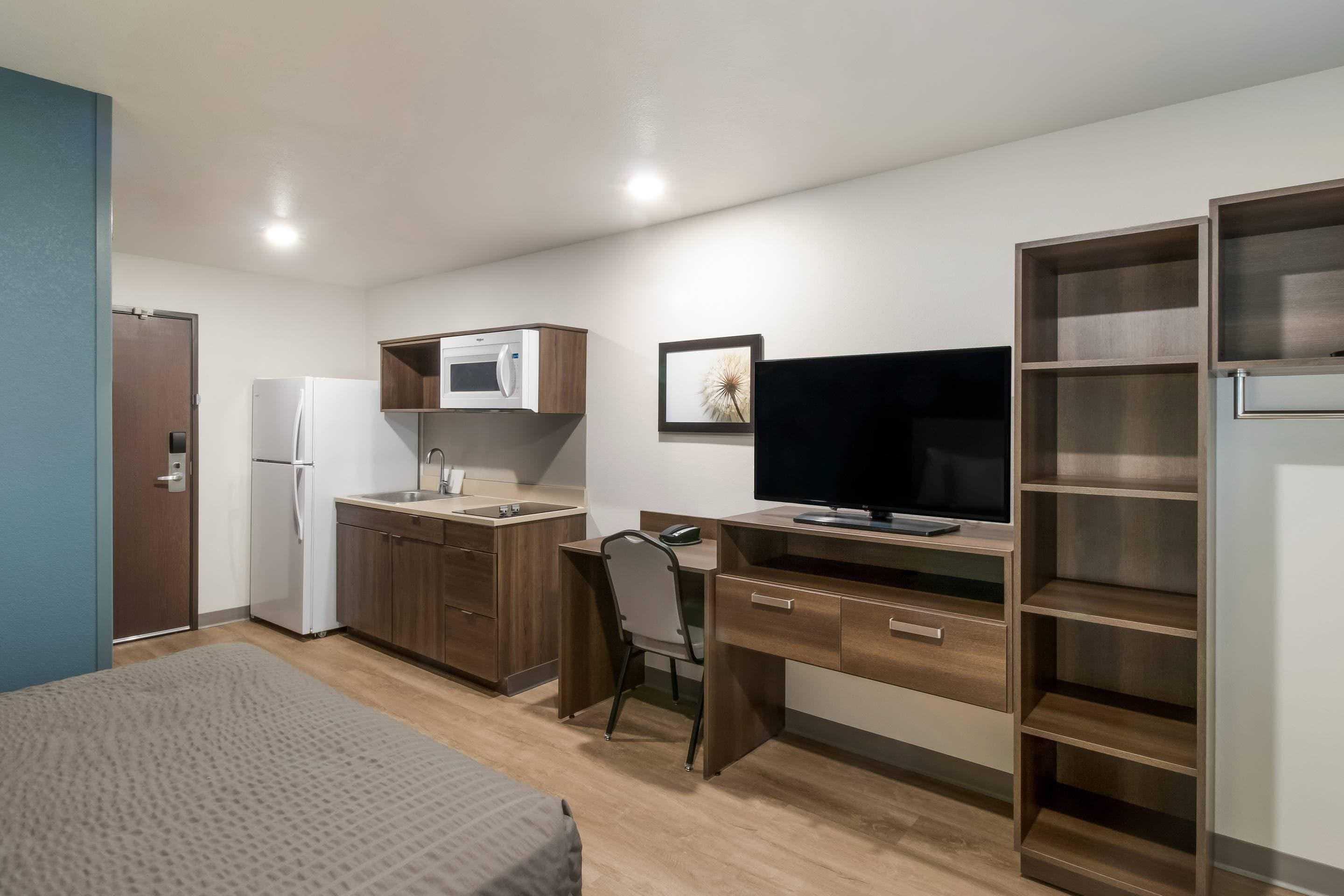 Une chambre de taille modeste comprenant un lit, un coin cuisine, un bureau avec une chaise, une télévision et une armoire.