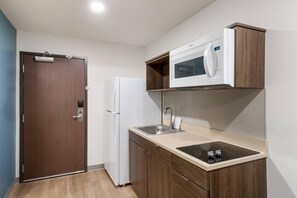 A compact kitchenette with a microwave, refrigerator, sink, and wooden cabinets. - Woodspring Suites Mesa Chandler (Mesa)