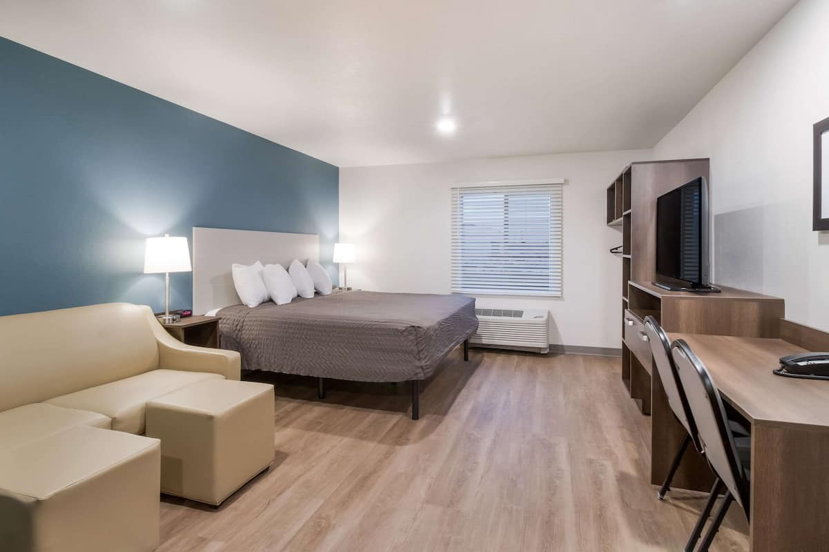 A modern hotel room with a bed, a sofa, a desk, and a TV.