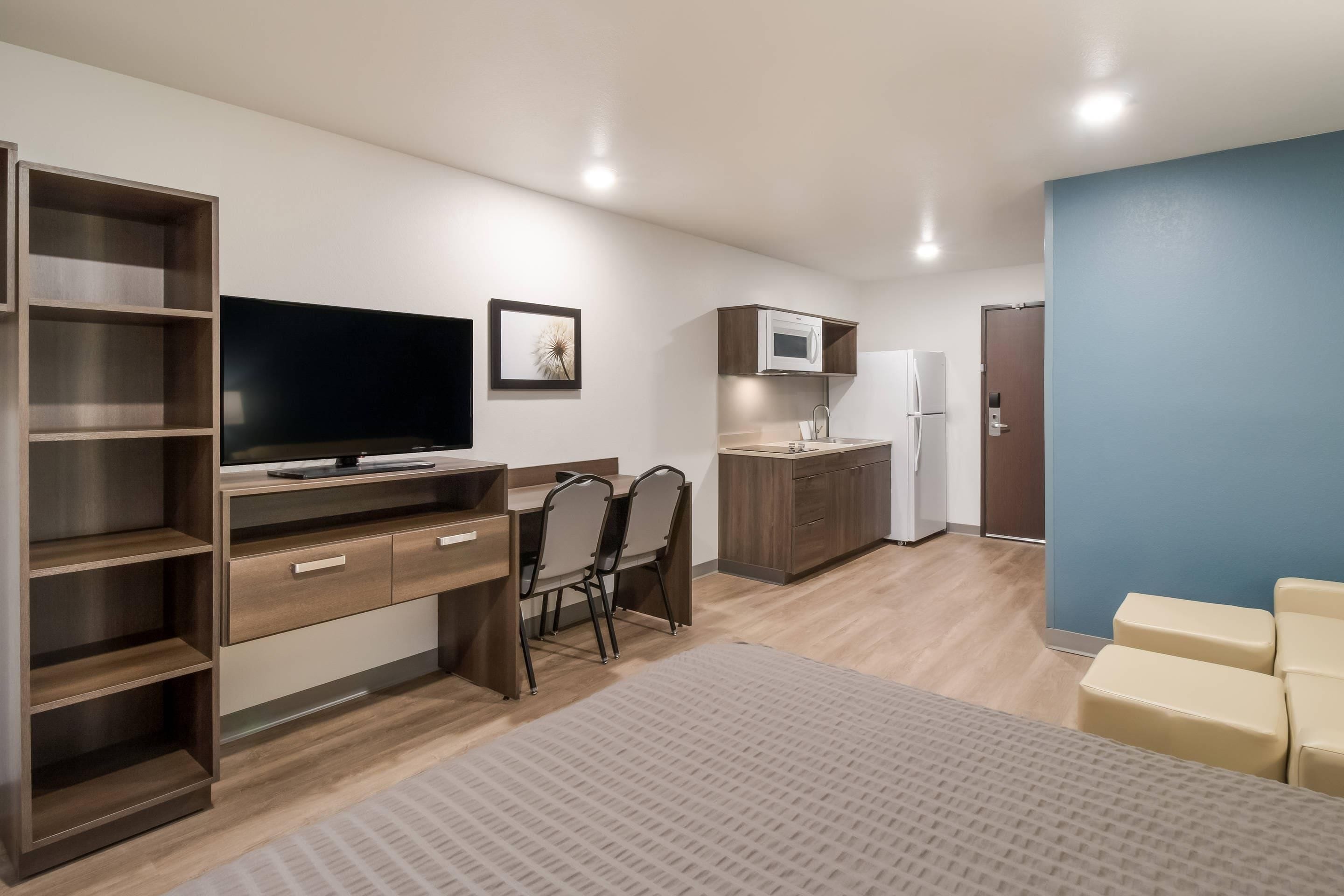 A modern bedroom with a bed, a desk, a television, a wardrobe, and a kitchenette.