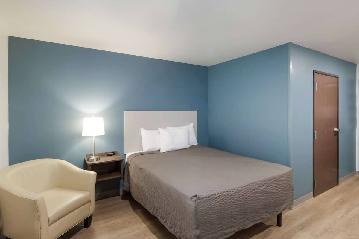 A bedroom with a bed, a nightstand, a lamp, a chair, and a door.