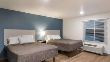 Habitación de hotel con dos camas, una mesita de noche con lámpara, una ventana con persianas y aire acondicionado instalado en la pared.