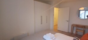 A bedroom with a bed, a wooden chair, a wardrobe, and a mirror on the wall.