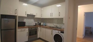 A compact kitchen with a refrigerator, oven, microwave, and washing machine.