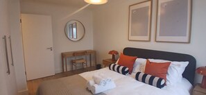 Une chambre d’hôtel avec un lit, un bureau, une chaise, un miroir rond et deux tableaux encadrés accrochés au mur.