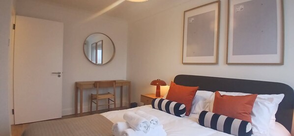Ein Hotelzimmer mit Bett, Schreibtisch, Sessel, rundem Spiegel und zwei gerahmten Bildern an der Wand.