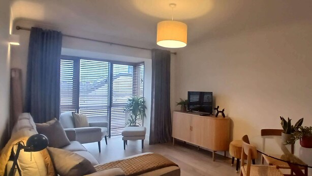 A living room with a sofa, ottoman, and a dining table with chairs. There is a TV on a stand and a plant on the table. - Stylish 2 Double Bed apartment in central Dublin (Dublin 1)