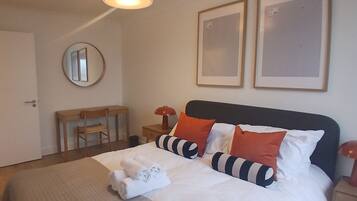 A hotel room with a bed, a desk, a chair, a round mirror, and two framed pictures on the wall.