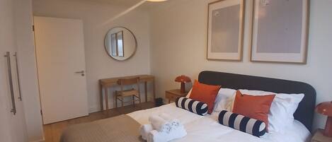 A hotel room with a bed, a desk, a chair, a round mirror, and two framed pictures on the wall.