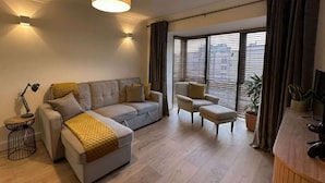 A modern living room with a sofa, armchair, and ottoman, a lamp, and a large window with blinds. - Stylish 2 Double Bed apartment in central Dublin (Dublin 1)