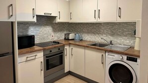 A modern kitchen with white cabinets, a microwave, stove, sink, and a washing machine. - Stylish 2 Double Bed apartment in central Dublin (Dublin 1)