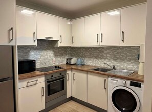 A modern kitchen with white cabinets, a microwave, stove, sink, and a washing machine.