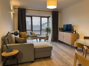 A modern living room with a sofa, armchair, dining table, and TV.