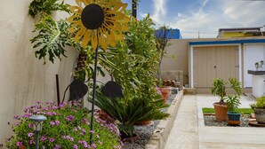 A garden with various plants and a large sunflower decoration. - Quality Lodging by the Sea. Lovely full size apartment w/balcony and ocean view. (Ensenada)