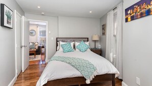 Un dormitorio con una cama de madera, ropa de cama blanca y un cuadro de un paisaje urbano en la pared.