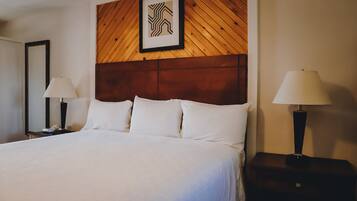 A hotel room with a large bed, two bedside tables with lamps, a wooden headboard, and a framed picture above the bed.