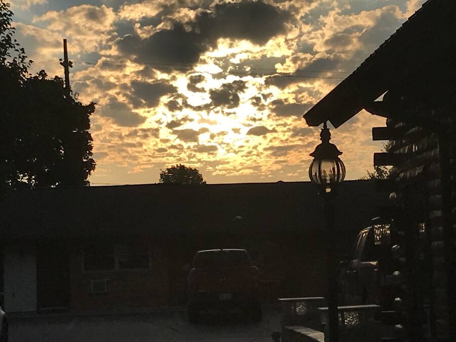 Un coucher de soleil avec des nuages, une voiture et un bâtiment avec un lampadaire.