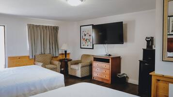 A hotel room with two beds, a television, a desk, a chair, a lamp, and a framed picture on the wall.