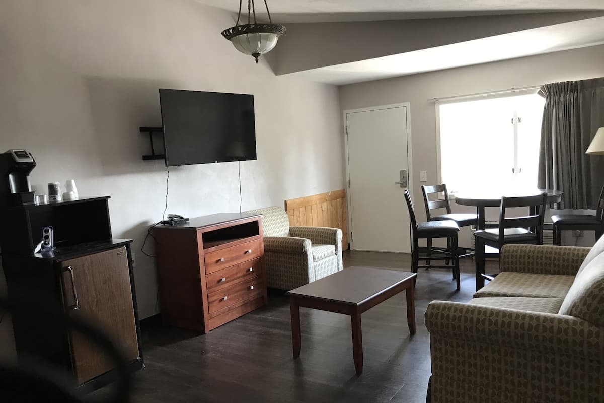 Una sala de estar con televisor de pantalla plana, muebles de madera, una mesa de comedor con sillas y una ventana con cortinas.