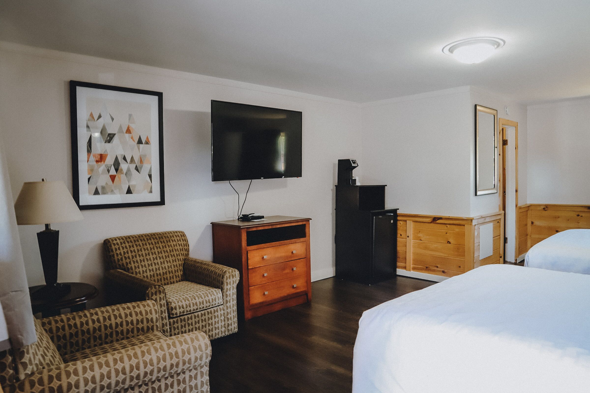 A hotel room with a bed, a chair, a dresser, a TV, and a framed picture on the wall.