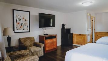 A hotel room with a bed, a chair, a dresser, a TV, and a framed picture on the wall.