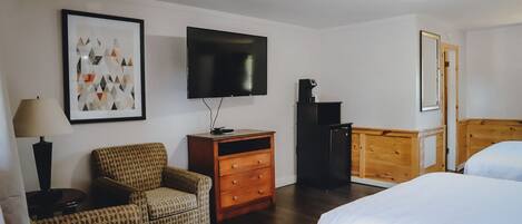 A hotel room with a bed, a chair, a dresser, a TV, and a framed picture on the wall.