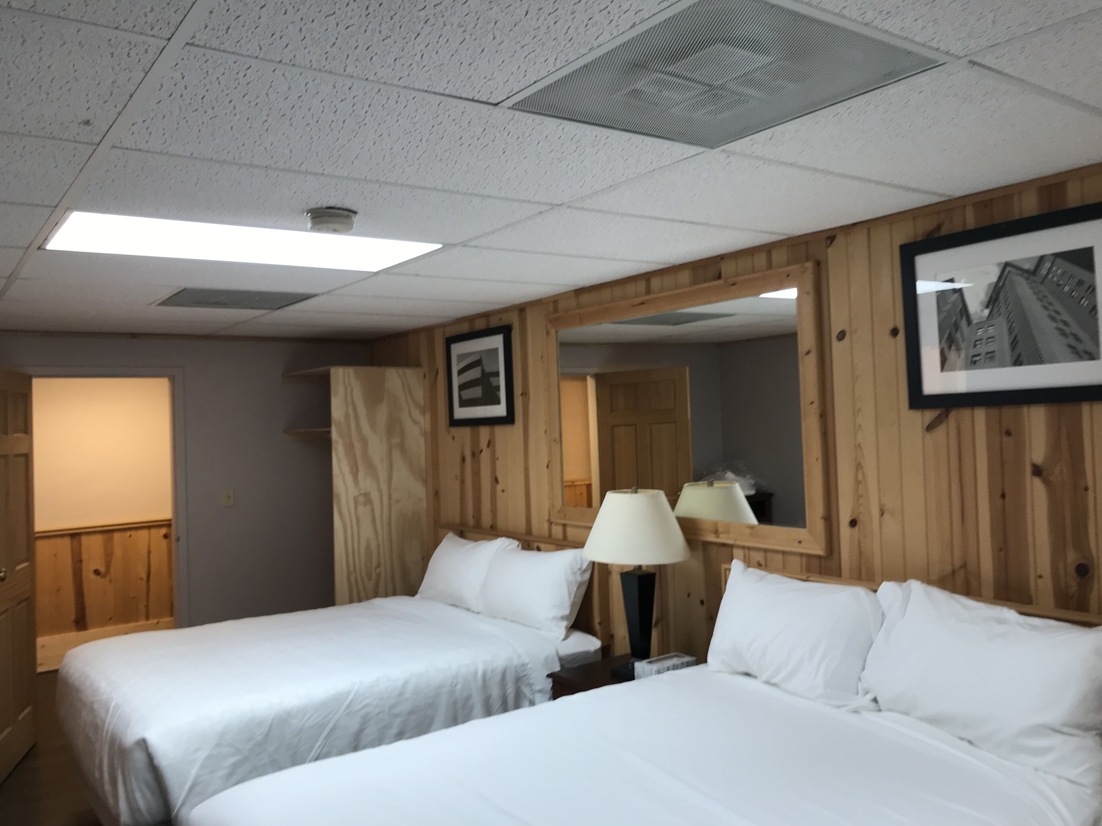A hotel room with two beds, a wooden headboard, a large mirror, and a framed picture on the wall.