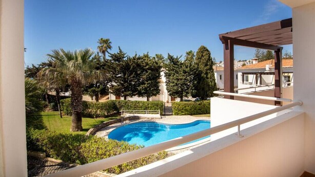 A balcony with a view of a swimming pool surrounded by greenery and trees.
