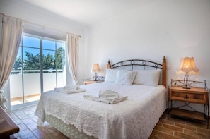 A bedroom with a large bed, two bedside lamps, a wooden nightstand, and a view of the outdoors through a sliding glass door.